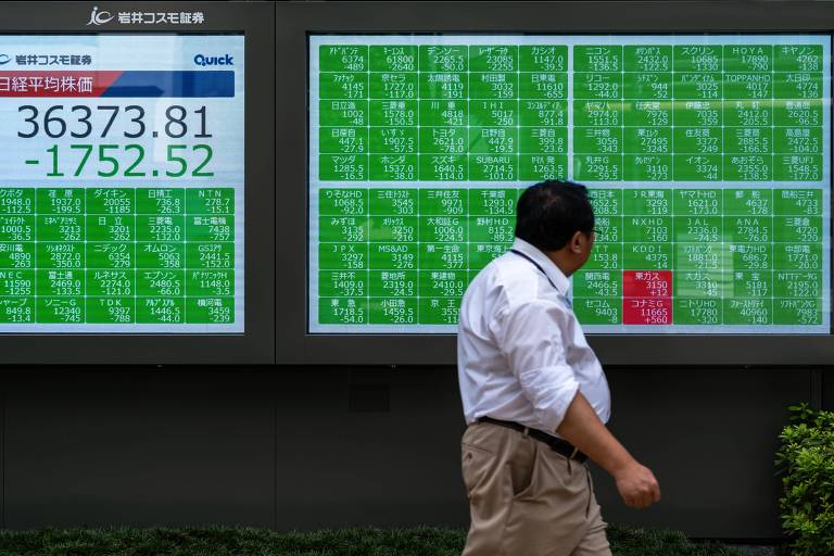 Homem caminha em frente a monitores que mostram números da bolsa de valores japonesa 
