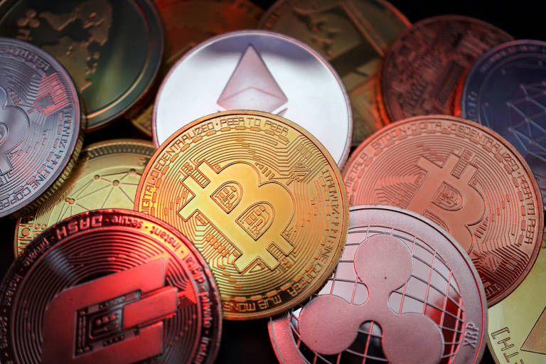 A imagem mostra várias moedas de criptomoedas dispostas em uma superfície. Entre elas, destacam-se moedas com os símbolos do Bitcoin e do Ethereum, além de outras criptomoedas. A iluminação cria um efeito de brilho nas moedas, que têm diferentes cores e designs.