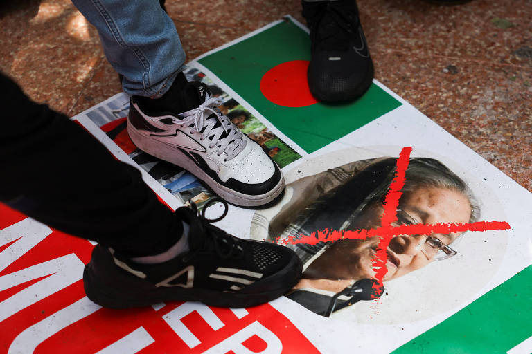 A imagem mostra pessoas pisando em um cartaz no chão. O cartaz contém uma foto de uma mulher com um 'X' vermelho sobre o rosto, indicando desaprovação. O fundo do cartaz é colorido, com predominância de verde e vermelho, e há palavras visíveis que parecem estar relacionadas a um protesto.