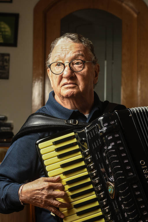 Retrato de Caçulinha tocando seu acordeon Valerio em seu apartamento em São Paulo