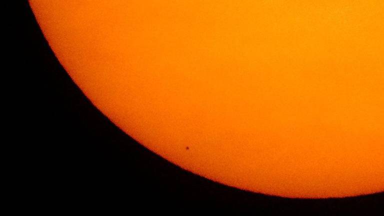 A imagem mostra um pequeno ponto preto na parte inferior de uma imensa bola laranja que é o sol