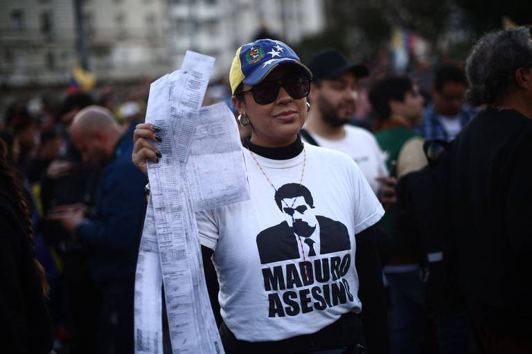 Manifestante usa camiseta com rosto de Nicolás Maduro e a frase 'Maduro assassino' enquanto segura folhas que imitam atas eleitorais durante protesto de imigrantes venezuelanos em Buenos Aires, na Argentina