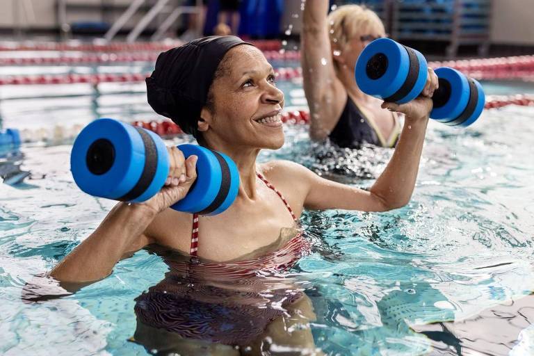 Mulher idosa levantando pesos dentro de uma piscina