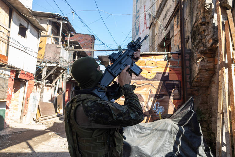 A imagem mostra um soldado vestido com uniforme militar e máscara, segurando uma arma em posição de disparo. Ele está em uma rua estreita cercada por edifícios de aparência deteriorada, com fios elétricos visíveis no céu