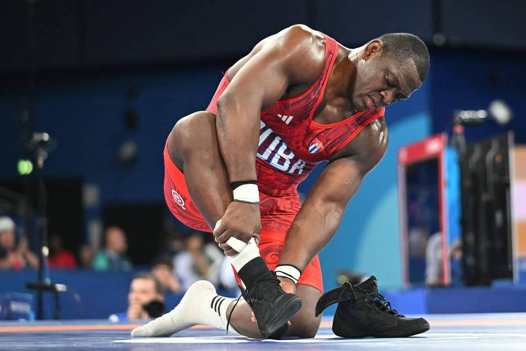 Com uniforme vermelho, o cubano Mijaín López tiras seus calçados depois de ganhar o ouro na luta greco-romana em Paris-2024, sua quinta conquista olímpica na mesma prova