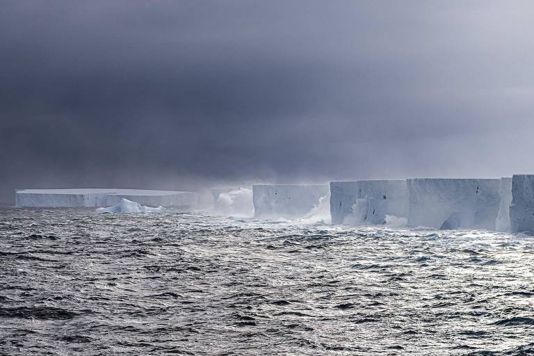 Iceberg enorme, com o topo plano, no mar sob um céu cinza escuro