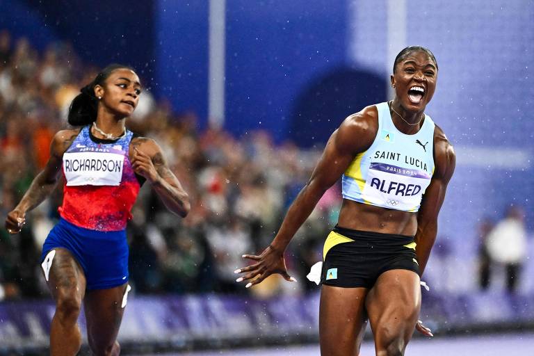 A imagem mostra duas atletas competindo em uma corrida. A atleta à frente, com um sorriso largo, está vestindo um uniforme amarelo e branco, enquanto a atleta atrás, com uma expressão de esforço, usa um uniforme azul e vermelho. O fundo é desfocado, sugerindo um ambiente de competição com uma multidão.