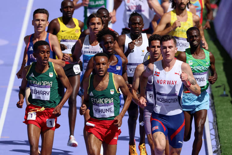 Um grupo de atletas competindo em uma corrida em uma pista. Os corredores estão em movimento, com alguns usando uniformes coloridos. A cena mostra uma variedade de expressões faciais e posturas, indicando esforço e concentração. O ambiente é ao ar livre, com uma pista visivelmente marcada.