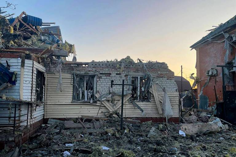 Com um céu de aurora ao fundo, imagem mostra casas parcialmente destruídas e escombros no chão