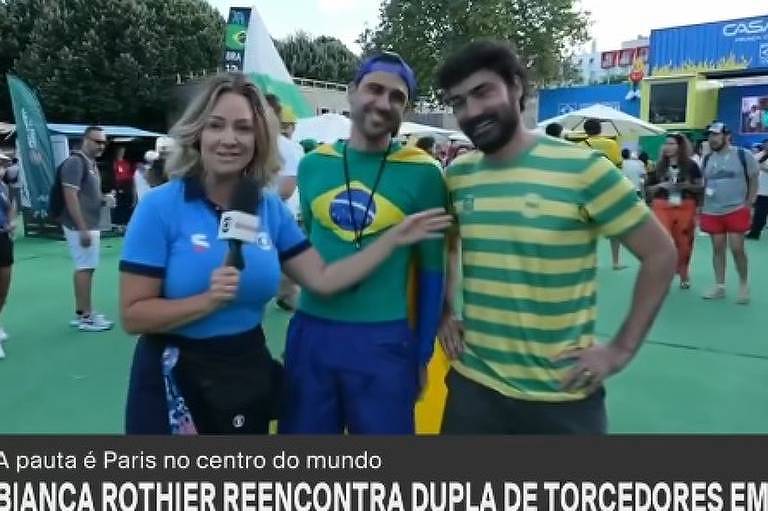 Mulher com microfone ao lado de dois homens vestindo as cores verde e amarelo