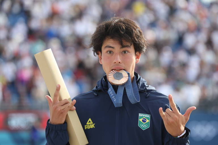 Com os olhos arregalados, Augusto Akio morde a medalha de bronze que ganhou no skate park nas Olimpíada de Paris