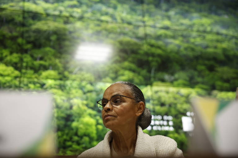 Retrato de Marina com um painel verde com fotografia de florestas ao fundo