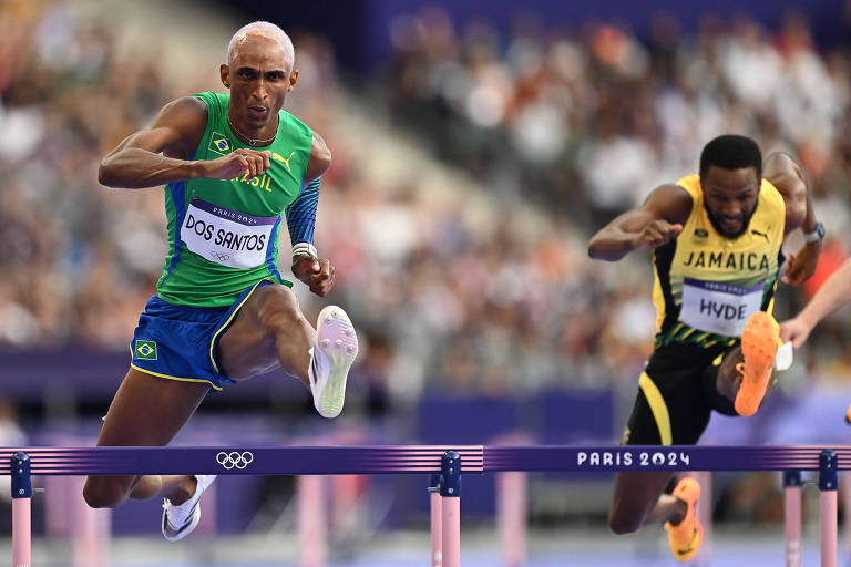 O brasileiro Alison dos Santos, o Piu, salta em semifinal dos 400 m com barreiras no Stade de France, em Saint-Denis, sede das provas do atletismo nas Olimpíadas de Paris; ao lado dele, atleta da Jamaica salta barreira