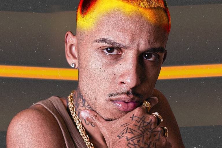 A imagem mostra um homem com cabelo curto e colorido, apresentando uma transição de amarelo para laranja na parte superior. Ele está usando uma camiseta sem mangas e possui vários anéis e colares. O homem tem tatuagens visíveis no pescoço e na mão, e está olhando diretamente para a câmera com uma expressão séria, apoiando o queixo com a mão.