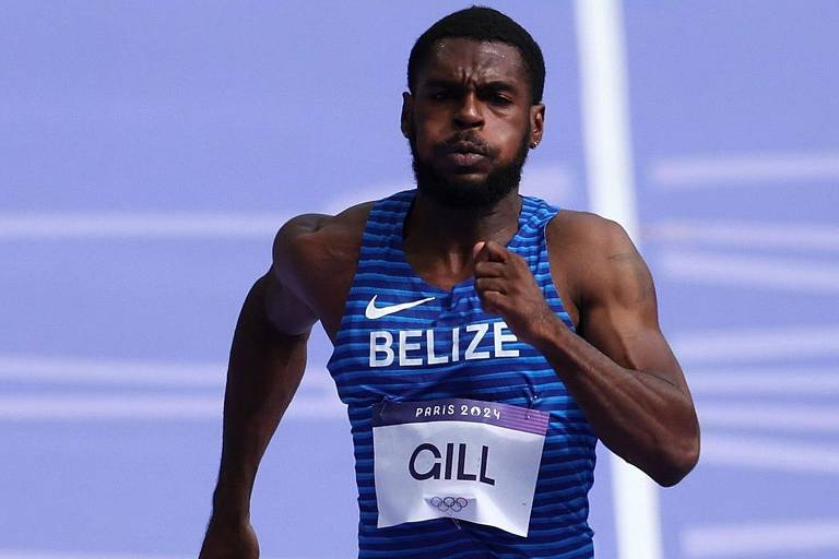 Um atleta está correndo em uma pista de atletismo. Ele usa uma camiseta azul com listras e o nome 'BELIZE' estampado. O atleta tem um olhar concentrado e está em movimento, com os músculos do braço visíveis. A placa em seu peito exibe o nome 'GILL' e a inscrição 'PARIS 2024'. O fundo é de uma pista de atletismo com um tom de azul.
