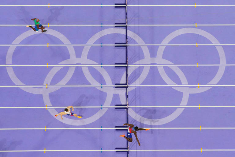 Imagem aérea de uma pista de atletismo com os anéis olímpicos desenhados no centro. Quatro atletas estão correndo em diferentes raias, com um fundo roxo. A pista possui linhas amarelas que delimitam as raias.