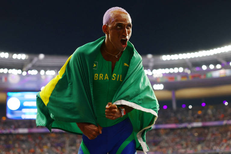 Com a bandeira do Brasil nas costas, Alison dos Santos, o Piu, vibra com a conquista nos 400 m com barreiras na final olímpica de Paris-2024 no Stade de France