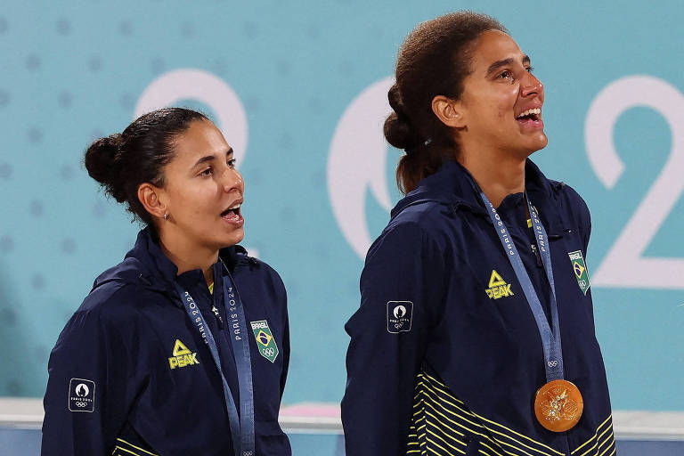 Medalhistas olímpicas de ouro no vôlei de praia, as brasileiras Duda e Ana Patrícia cantam o hino nacional no pódio da Arena da Torre Eiffel, em Paris