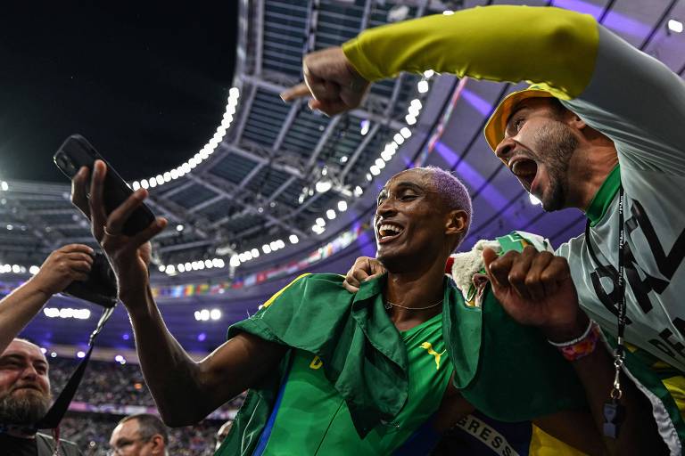 Sorrindo, Alison dos Santos, medalhista de bronze nos 400 m de barreiras nas Olimpíadas de Paris, tira selfie com torcedor no Stade de France