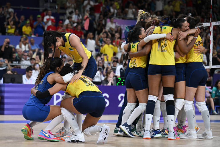 A imagem mostra jogadoras da equipe de vôlei feminino do Brasil comemorando uma vitória. Algumas jogadoras estão se abraçando, enquanto outras estão agachadas, expressando alegria e emoção. O fundo é uma multidão de torcedores, com bandeiras e camisas nas cores da seleção brasileira. O ambiente é de celebração e entusiasmo.
