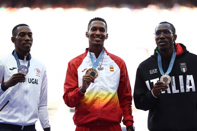 Três atletas estão no pódio durante uma cerimônia de premiação. O atleta à esquerda veste uma jaqueta branca com detalhes em vermelho e azul, representando Portugal. O atleta do meio usa um uniforme vermelho e amarelo, representando a Espanha, e segura uma medalha de ouro. O atleta à direita está vestido com uma jaqueta preta com a palavra 'ITALIA' em branco, representando a Itália, e segura uma medalha de bronze.