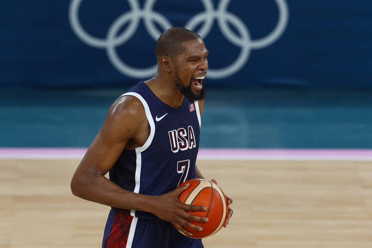 Segurando a bola de basquete com as duas mãos, o ala-pivô norte-americano Kevin Durant vibra durante a decisão do ouro das Olimpíadas de Paris, contra a França, na Arena Bercy