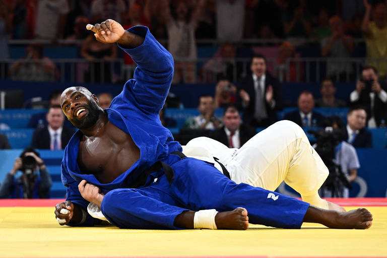 Usando quimono azu, o judoca francês Teddy Riner vibra, sorrindo, no tatame da Arena do Campo de Marte ao derrotar por ippon o japonês Tatsuru Saito na final por equipes mistas das Olimpíadas de Paris