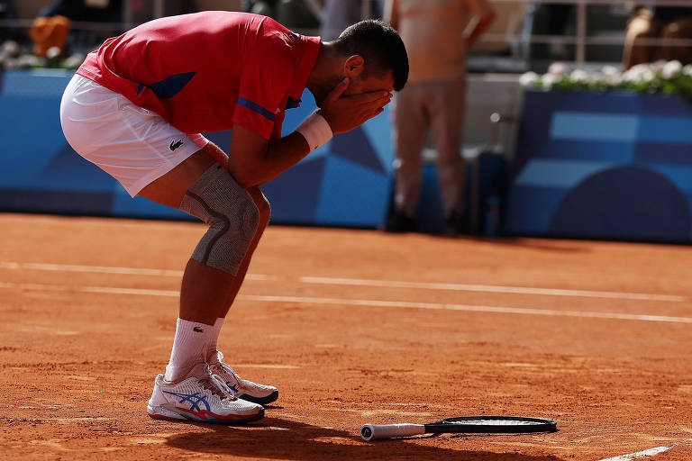 O sérvio Novak Djokovic leva as mãos ao rosto depois de ganhar a final do tênis dos Jogos Olímpicos de Paris-2024, contra o espanhol Carlos Alcaraz, em Roland Garros