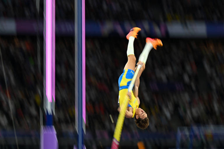 O sueco Armand Duplantis fica de cabeça para baixo ao executar movimento para cravar o novo recorde mundial na final do salto com vara das Olimpíadas de Paris, no Stade de France