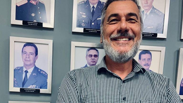 Homem branco de camisa xadrez encostado a uma galeria de fotos de homens fardados