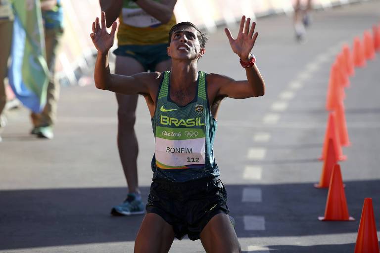 Caio Bonfim se ajoelha e olha para o alto, com as mãos erguidas e espalmadas, ao completar os 20 km da marcha atlética em segundo lugar e ganhar a medalha de prata nas Olimpíadas de Paris