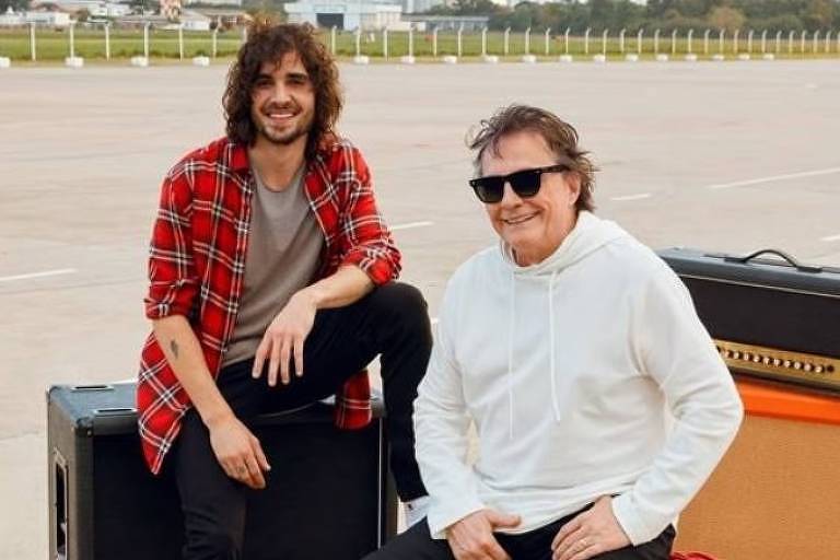 Em foto colorida, dois homens posam juntos para uma campanha publicitária