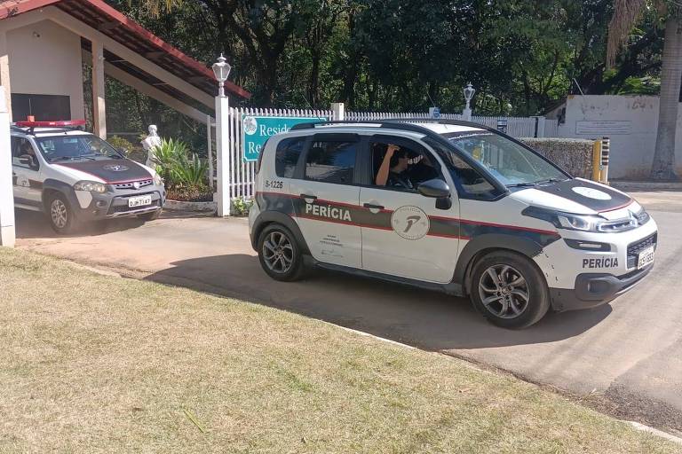 A imagem mostra dois veículos de perícia estacionados em frente a uma entrada de residência. O veículo da esquerda é um modelo SUV, enquanto o da direita é um carro compacto. Ambos têm a palavra 'PERÍCIA' escrita em destaque nas laterais