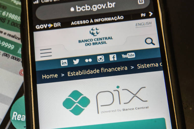 A imagem mostra um smartphone exibindo um aplicativo de pagamento com informações sobre uma transação, incluindo o valor de R$ 10,00, e o site do Banco Central do Brasil. O aplicativo apresenta detalhes como chave, saldo e informações do destinatário, enquanto o site contém o logotipo do Banco Central e opções de navegação.