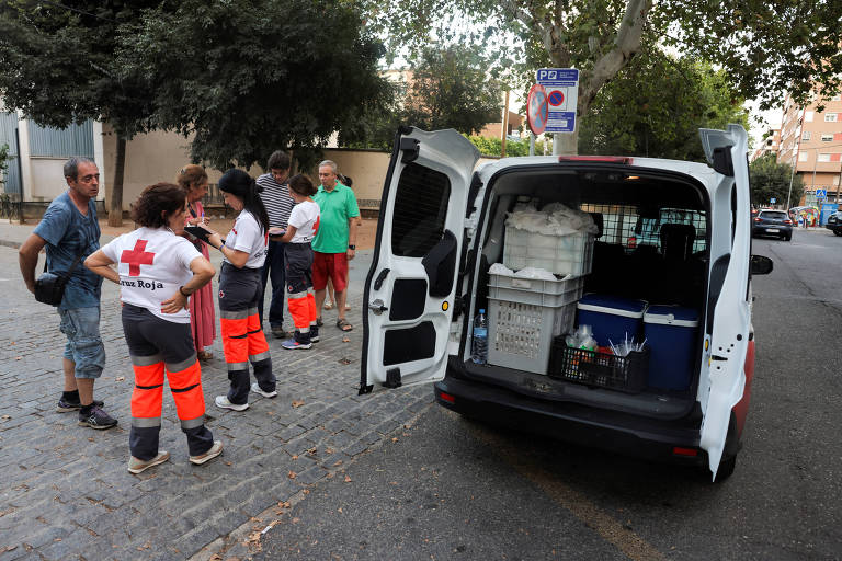 Ambulância estacionada em rua, com portas abertas, e algumas pessoas na calçada ao lado dela