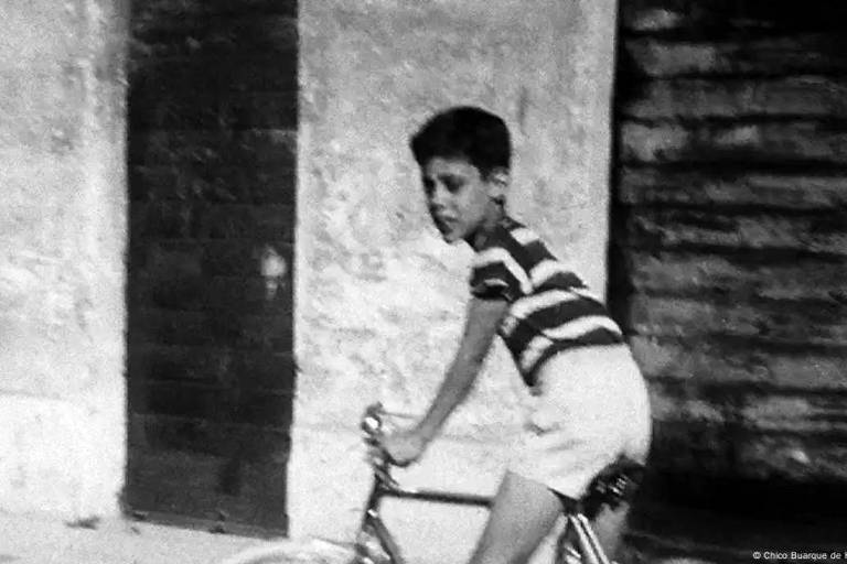 Foto: Chico Buarque de Hollanda Collection/Antônio Carlos Jobim Institute *** Local Caption *** A imagem em preto e branco mostra um menino montado em uma bicicleta. Ele está usando uma camiseta listrada em preto e branco e shorts claros