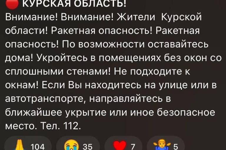 A imagem contém um aviso de emergência em russo para os residentes da região de Kursk, alertando sobre a ameaça de ataques de mísseis. O texto recomenda que as pessoas permaneçam em casa, se escondam em locais sem janelas e não se aproximem das janelas. Se estiverem na rua ou em transporte público, devem se dirigir ao abrigo mais próximo ou a um local seguro. O número de telefone para emergências é 112.