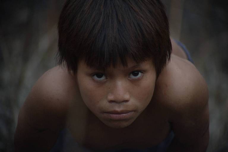 A imagem mostra um menino com cabelo curto e escuro, olhando diretamente para a câmera. 