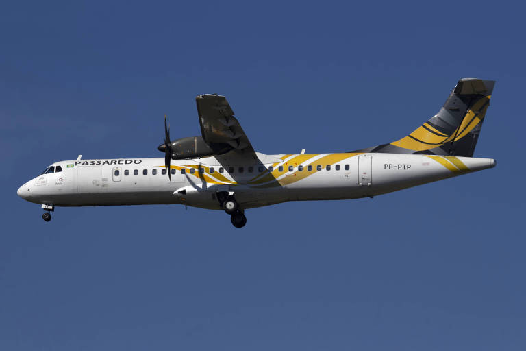 Imagem de um avião de passageiros em voo, com fuselagem branca e detalhes em amarelo e preto. O avião está posicionado lateralmente, com as hélices visíveis e um céu azul ao fundo.