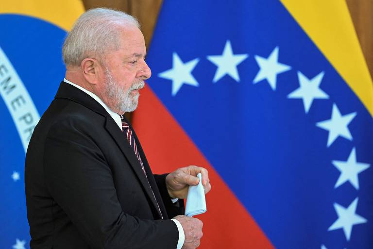 Lula é um homem branco idoso e está vestindo terno escuro e gravata, segurando um lenço, e caminha diante de bandeiras do Brasil e da Venezuela. O fundo apresenta as cores e símbolos das bandeiras, com destaque para as estrelas da bandeira venezuelana.