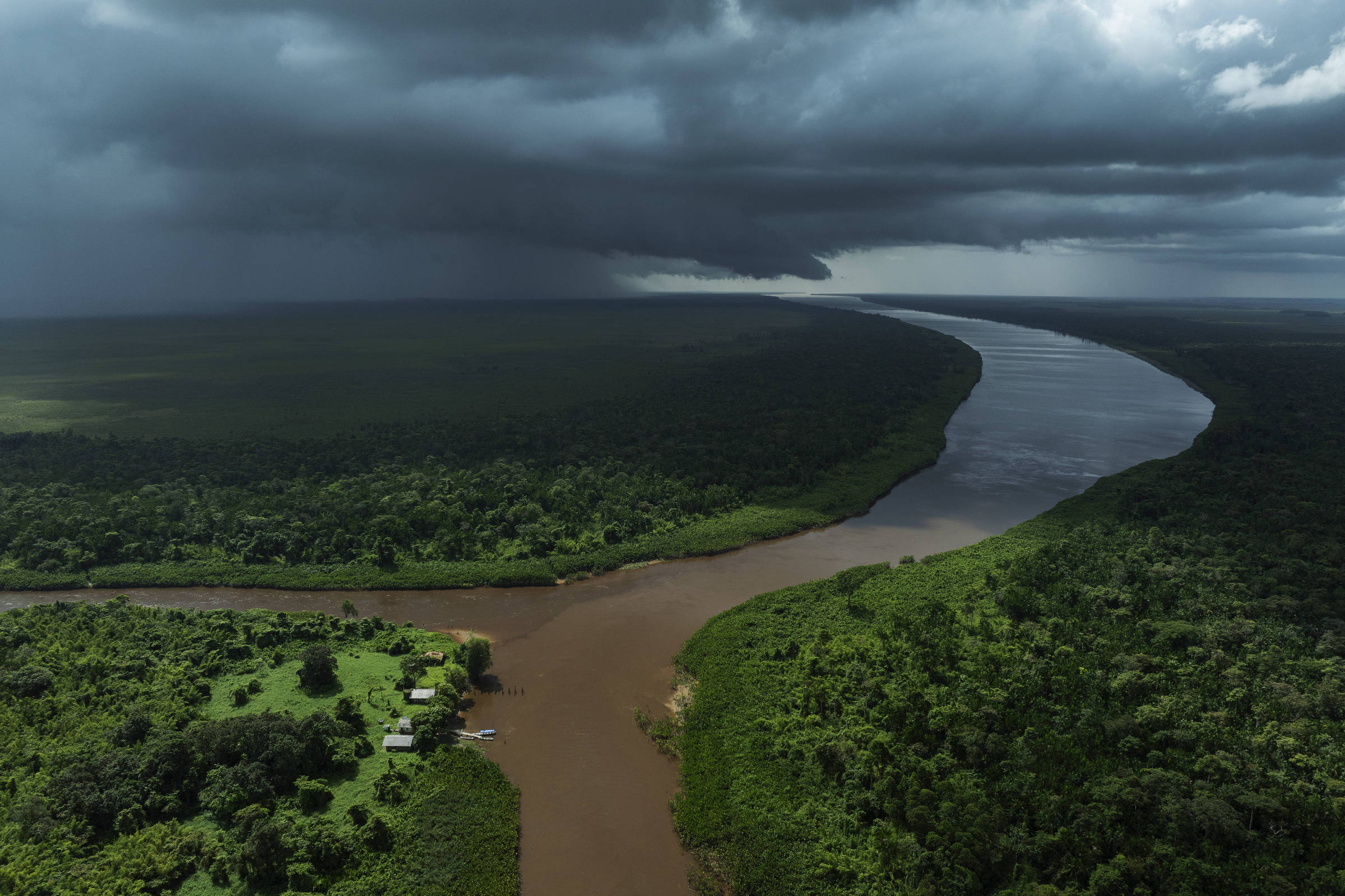 Vista de drone de rio em formato curvo que passa ao lado de três casas em local coberto de vegetação