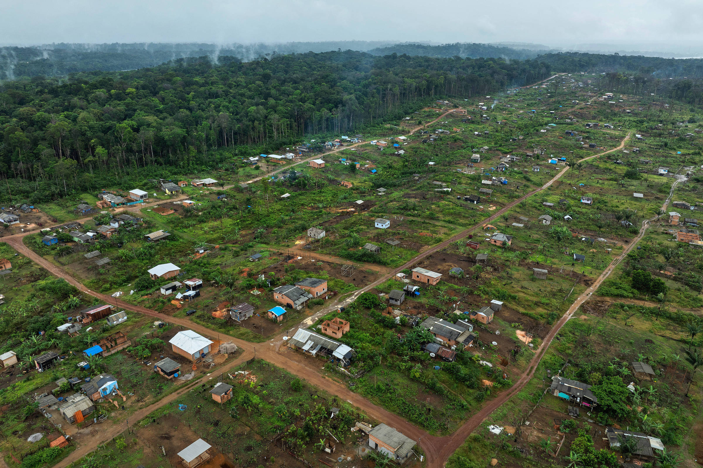 Vista de drone de casas pequenas em terreno desmatado ao lado de floresta