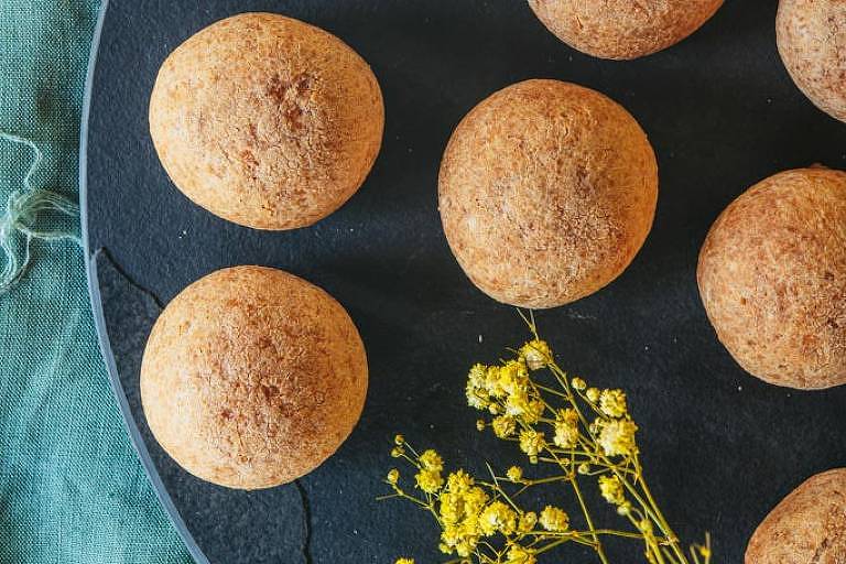 A imagem mostra alguns pães de queijo em um prato azul. Com eles, também está um galho de flor.