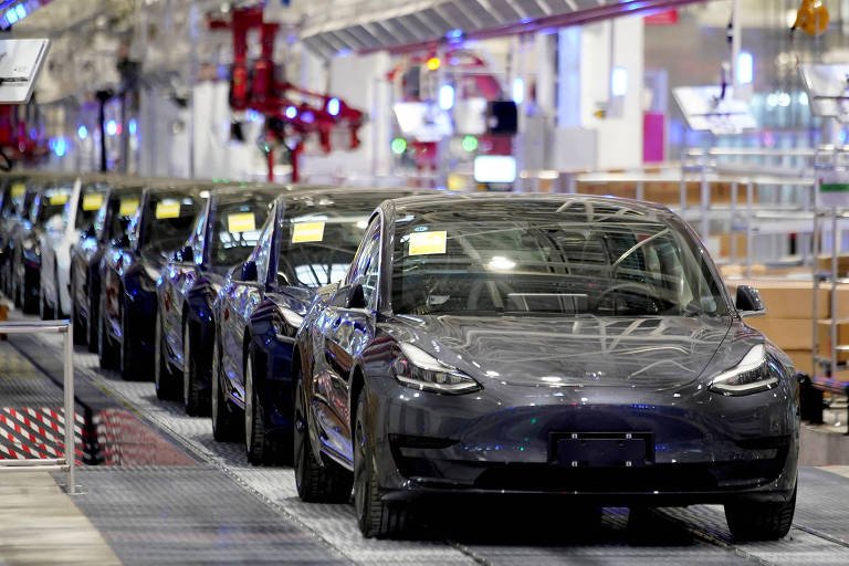 Fotografia mostra carros pretos enfileirados em um corredor de uma fábrica. O ambiente é iluminado com luz branca.