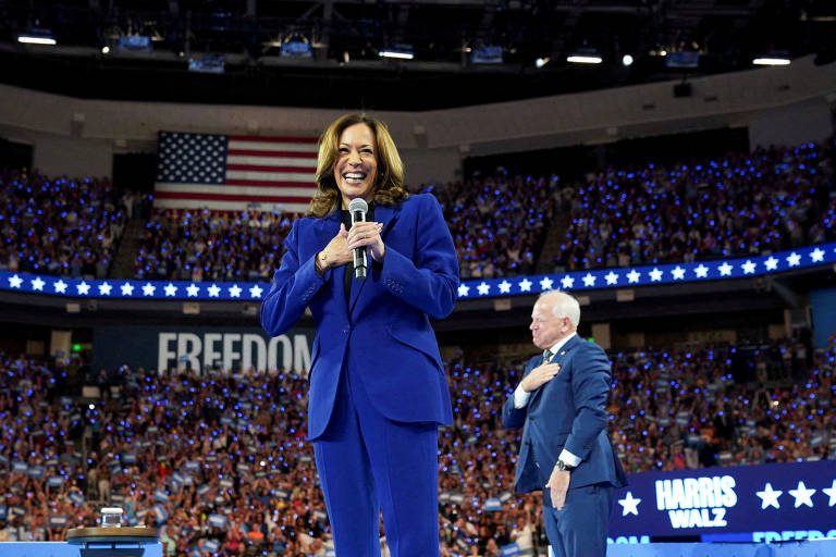 A vice-presidente dos EUA e candidata presidencial democrata, Kamala Harris, sorri para o público, enquanto seu companheiro de chapa, o governador de Minnesota, Tim Walz, saúda o outro lado da plateia, durante convenção em Chicago