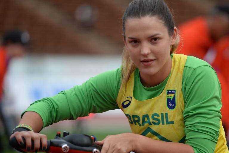 A imagem mostra uma jovem atleta sentada em um veículo de apoio, com uma expressão concentrada.