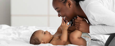 Speech And Language Development For Babies. Closeup profile portrait of beautiful little black infant smiling, young black woman playing and holding kid's legs in hands, banner, free copy space