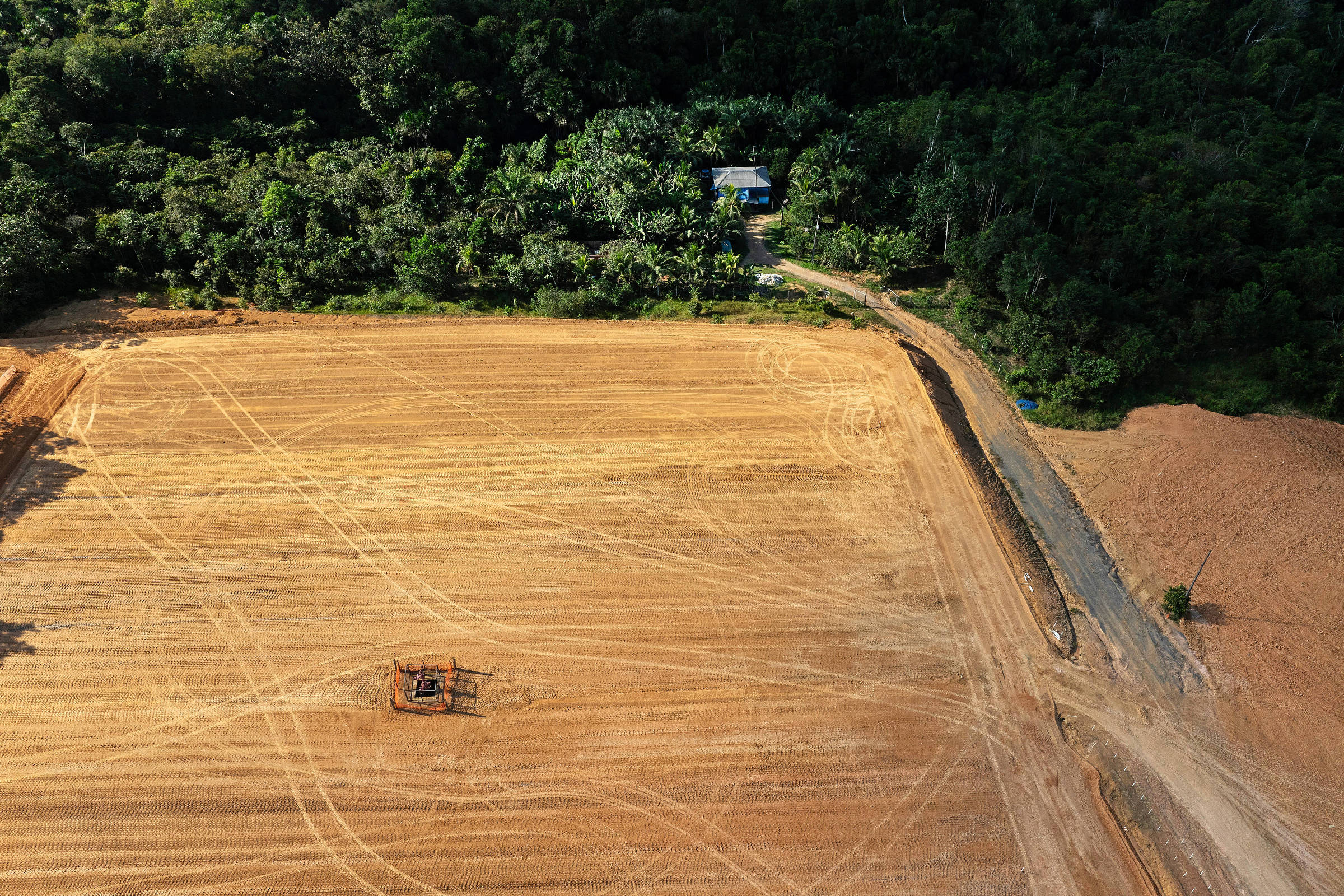 Vista de drone de terreno desmatado com um poço aberto e ao fundo uma casa cercada por mata