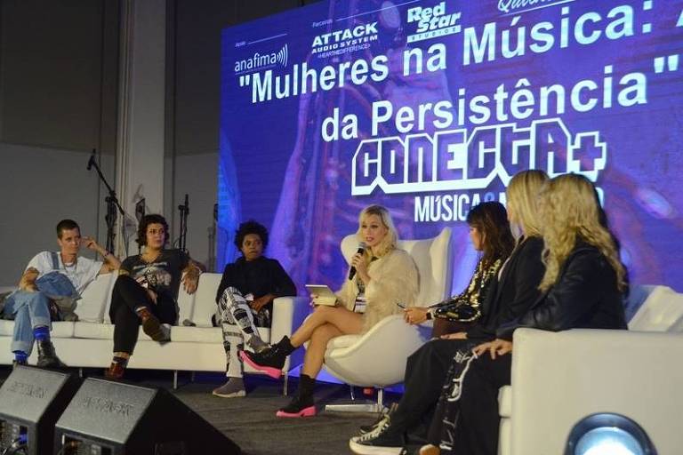 Em foto colorida, a cantora Bianca Jhordão aparece dando uma palestra em um palco