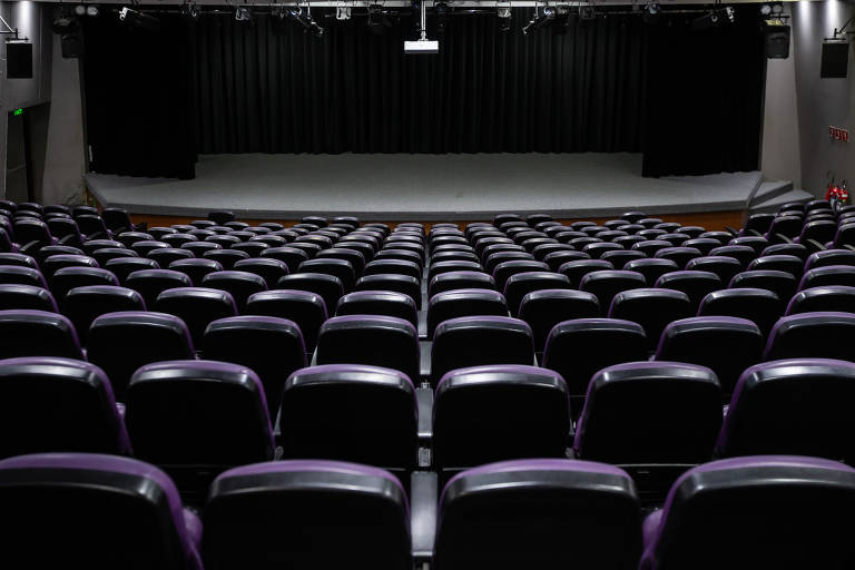 A imagem mostra o palco do Teatro Renaissance visto por tras de seus assentos com acolchoado roxo. O palco é cinza. O local está vazio.